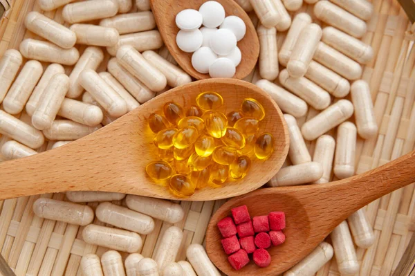 Sağlıklı yaşam tarzı, vitaminler, mineraller ve örülmüş bambu bir tabağın içindeki tahta kaşıklardaki besin takviyeleri. Üst Manzara. Yakın plan..