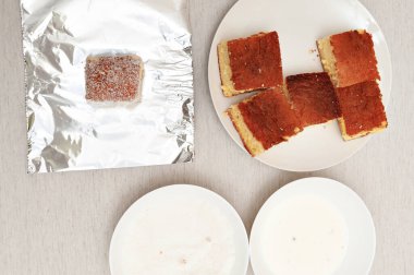 Portekizce BOLO GELADO olarak bilinen geleneksel Brezilya tatlısı- adım adım: kek parçaları, alüminyum folyo, sütlü tabaklar ve rendelenmiş hindistan cevizi. Üst görünüm.