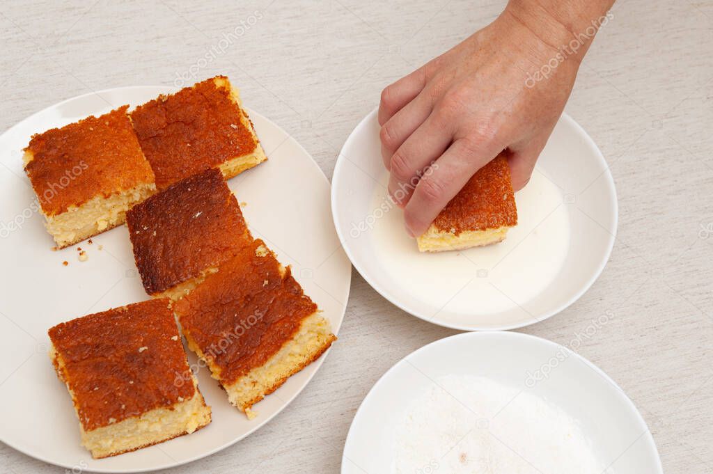 Traditional Brazilian dessert known as BOLO GELADO in Portuguese - Making step by step: Hand putting piece of cake in milk. Top view