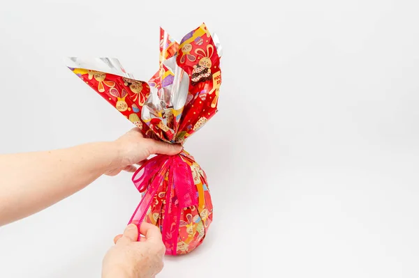 Easter Egg - Hands unpacking homemade chocolate egg with red ribbon. Isolated on white background with copy space.