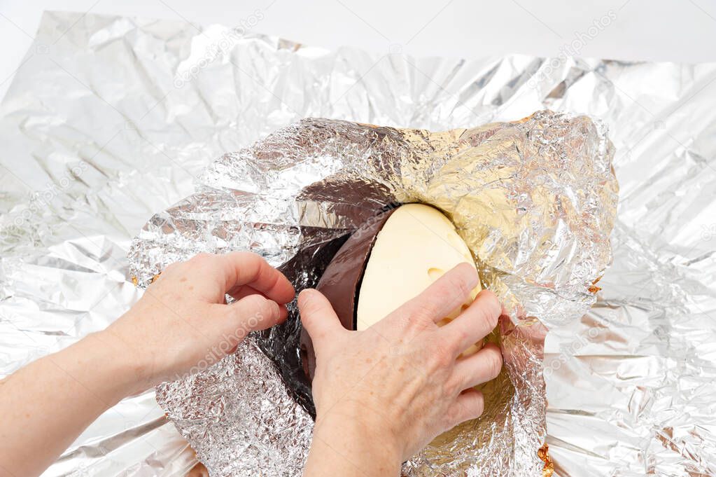 Easter Egg - Hands unpacking homemade chocolate egg wrapped in aluminum foil. Copy space.