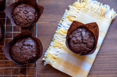 Tahta kesme tahtasının üzerinde kahverengi kağıt bardaklarda çikolatalı kekler.