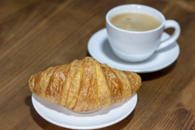 Ahşap arka planda kruvasan ve fincan kahve.