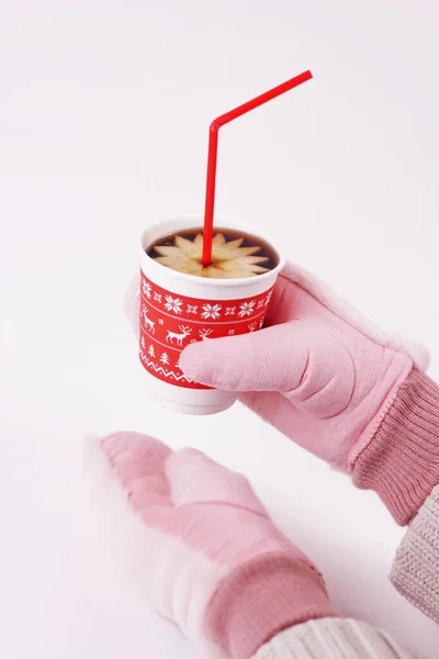 Gloved hands holding mug filled with hot beverage.Mulled wine in red paper cup with drinking straw on white background.Winter holiday christmas new year concept.