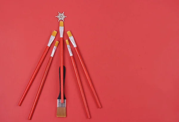 Kırmızı arka planda yaratıcı Noel ağacı, sanat brushes. xmas arka planında resim yapmak için araç gereçlerden yapılmış. Tebrik kartı ve yeni yıl konsepti..