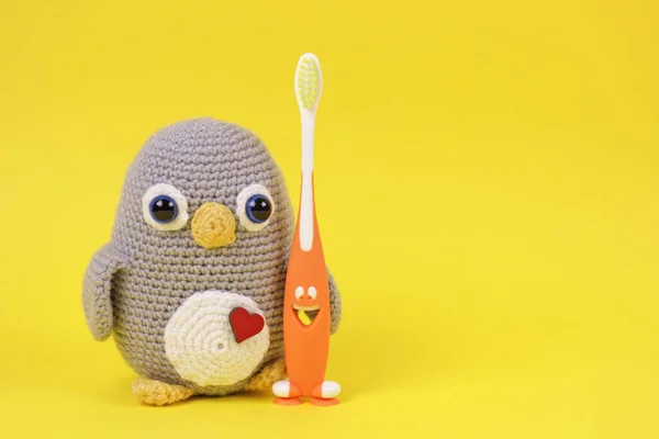 Krásná dětská scéna s ručně pletenou hračkou.Háčkování Amigurumi tučňák hračka se zubním kartáčkem na žlutém pozadí.Skvělé pro malé podniky, dětské bloggery, stránky sociální sítě, obchody, webové stránky. — Stock fotografie