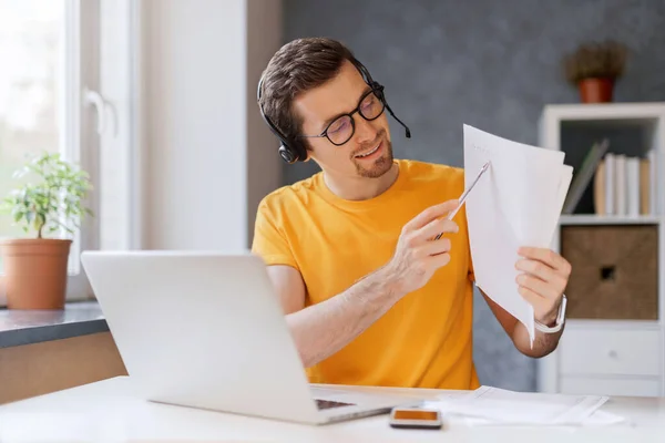 Millennial Profesyoneli çevrimiçi öğretmen bilgisayarını kullanarak online dil ya da matematik dersi veriyor ve egzersize işaret ediyor. Gülümseyen genç serbest çalışan kulaklık takıyor, video aracılığıyla müşteriyle iletişim kuruyor.
