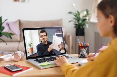 Genç öğretmen web kamerası kullanarak öğrenciyle görüntülü görüşme yapıyor. Dizüstü bilgisayarında özel öğretmeniyle çevrimiçi dersi olan bir kız. Uzaktan eğitim, e-öğrenme konsepti. Karantina, uzak öğrenim