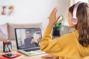 Evde eğitim gören küçük bir kız covid salgını nedeniyle okul öğretmeninden sanal internet dersini öğreniyor. Erkek öğretmen kulaklık ve webcam kullanarak matematik öğretiyor.