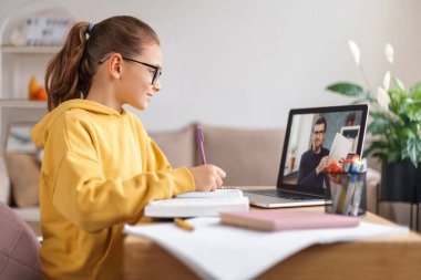 Liseli kız, evdeki oturma odasında dizüstü bilgisayarında öğretmeniyle video konferansı yapıyor. Evde eğitim, uzaktan öğrenme, koronavirüs salgınına bağlı online eğitim. Yan görüş. E-öğrenme kavramı