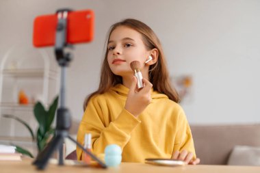 Gülümseyen kız blogcu evde video kaydediyor, masadaki akıllı telefona bakıyor, online ders çekimi yapıyor, kozmetik nasıl kullanılır, web kamerasında makyaj yapıyor. Çocuk sosyal medya kavramı