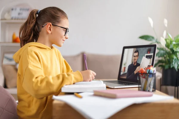 Liseli kız, evdeki oturma odasında dizüstü bilgisayarında öğretmeniyle video konferansı yapıyor. Evde eğitim, uzaktan öğrenme, koronavirüs salgınına bağlı online eğitim. Yan görüş. E-öğrenme kavramı