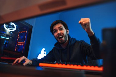 Genç profesyonel oyuncunun yakın plan portresi çevrimiçi video oyunu kazanmaktan memnun, EVET el hareketi gösteriyor, gülümsüyor. Çıkan erkek siber sporcu turnuvayı kazandı ve zaferi kutladı. Sanal spor