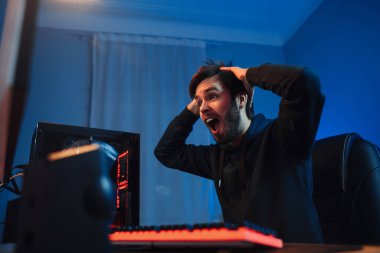 Genç erkek siber sporcu portresi çevrimiçi turnuva ya da atıcı video oyunu kazanmakla şok oldu, ellerini başının üstünde tutuyor, heyecanlanıyor. Yan görüş, neon ışık, yakın çekim. Profesyonel siber spor