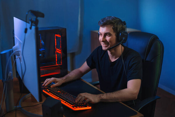 Молодой профессионал играет в онлайн-видеоигры на своем компьютере. Он улыбается, потому что выигрывает игру, имея прямой эфир для своих подписчиков и подписчиков. Концепция киберспорта. Командная игра