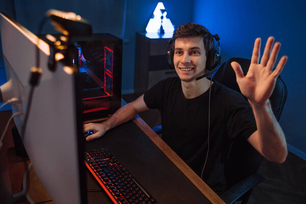 Профессиональный кибер-геймер, имеющий прямой эфир, машущий рукой последователям и подписчикам своего интернет-канала, записывающий видео через веб-камеру во время игры в онлайн-видео-игру в комнате. Неоновый цвет фона
