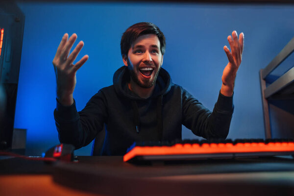 Портрет мужчины-профессионального геймера выиграл онлайн-видеоигру, держит руки поднятыми, взволнованным, довольным победой в электронном спортивном турнире, играя по ночам дома. Киберспорт, современные технологии, развлечения