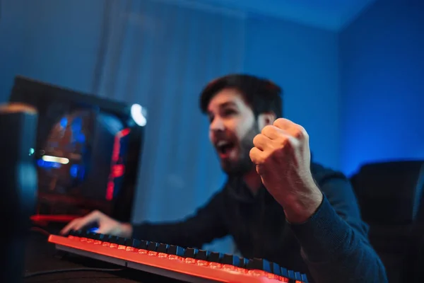 Professional Gamer Playing and Winning in Shooter Computer Video Game. Neon Lights, side view. Cyber sport player won online tournament, feel exited and happy, shows YES gesture. Computer addiction