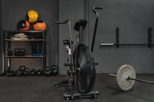 Empty crossfit gym with sports equipment: air bike, barbell, kettlebells, dumbbells, weighted balls, battle ropes. Copy space. Workout, bodybuilding and fitness content