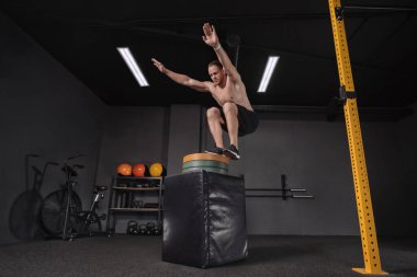 Crossfit sporcu, karanlık spor salonunda atlama egzersizi yapıyor. Kaslı, formasız, kaslı bir adam bacak egzersizi yapıyor. Crossfit, fitness, egzersiz