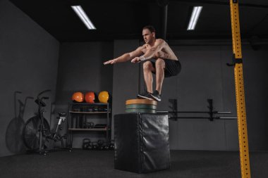 Atletik bir adamın kutu atlayışı egzersizi yaparken portresi. Crossfit, spor ve sağlıklı yaşam tarzı kavramı. Egzersiz rutininin bir parçası olarak genç bir trenin kutuya atlaması. Cross, işlevsel eğitim