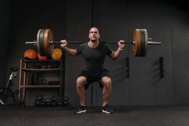 Kas gevşetici sporcu, koyu renk spor salonunda halterle ağırlık kaldırıyor. Spor kulübünde ağırlık kaldıran bir adam, fonksiyonel bir eğitim dersi var, spor yapıyor.