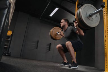 Kaslı beyaz adam ağırlık kaldırıyor ve spor salonunda çömeliyor. Crossfit sporcusu çömelirken omuzunda ağır bir halter tutuyor. Spor ve spor