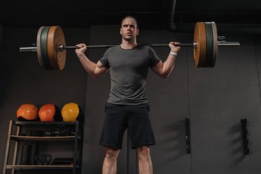 Spor salonunda ağırlık kaldırma halteriyle kaslı, vahşi sporcu eğitimi. Güçlü kaldırma, halter, fonksiyonel eğitim konsepti. Crossfit sporcu ağırlık kaldırıyor ve sırt üstü çömeliyor.