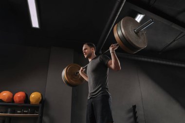 Fitness adamı halterle ağırlık çalışması yapıyor. Genç kaslı sporcu karanlık spor salonunda antrenman yapıyor. Vücut geliştirici ağırlık kaldırıyor. Crossfit konsepti
