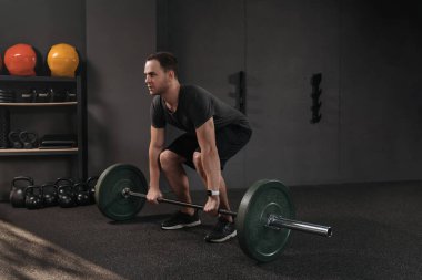 Crossfit atlet ağırlık kaldırırken halter kaldırmaya hazırlanıyor. Formda genç bir adam ağırlık kaldırıyor, spor salonunda çalışıyor. Karanlık arka plan. Spor, spor, kaldırma konsepti