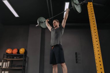 Crossfit sporcusu halterle kafasının üstünde çömeliyor. Spor salonunda halteri kaldıran genç kaslı adamın portresi. Ağırlık kaldırma, ağırlık kaldırma ekipmanları. Spor, spor - sağlıklı yaşam tarzı konsepti.