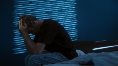 Stresli bir adam geceleri karanlık bir odada yatağın kenarına oturur ve başı derttedir. Depresyon, tükenme ya da zihinsel sağlık sorunları. Boşluğu kopyala