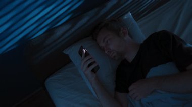 Yorgun genç adam gece yatağında uzanıyor, akıllı telefon ekranına bakıyor, sosyal medyada kıyamet kopuyor, uyku düzensizliği ya da dikkat dağınıklığıyla fazla düşünerek uyuyamıyor. Boşluğu kopyala