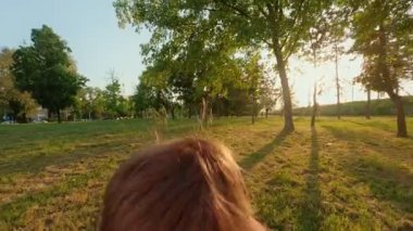 Güneşli bir günde gökyüzü ve ağaçlarla kaplı bir ebeveyn tarafından terk edilirken neşeli bir şekilde gülümseyen heyecanlı genç çocuk. POV bakış açısı, bir babanın yüksekten atması ve gülen oğlunu parkta yakalaması..