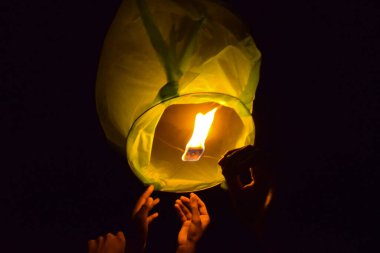Hands letting go a lightened up sky lantern to the black night sky in celebration of festival