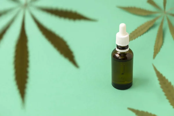 stock image Green marijuana leaves on green background with cannabis oil in a glass bottle, selective focus