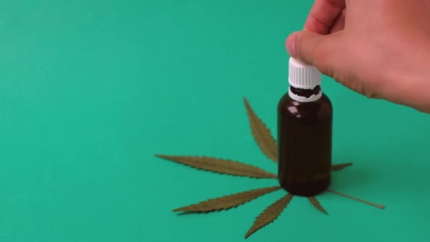 Frau nimmt Pipettentropfen mit Cannabis-Öl auf grünem Hintergrund mit Marihuana-Blatt — Stockvideo