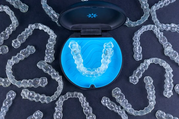 Plastic case with invisible transparent orthodontic retainers invisalign on black background. Aligner brackets or braces dental container — Stock Photo, Image