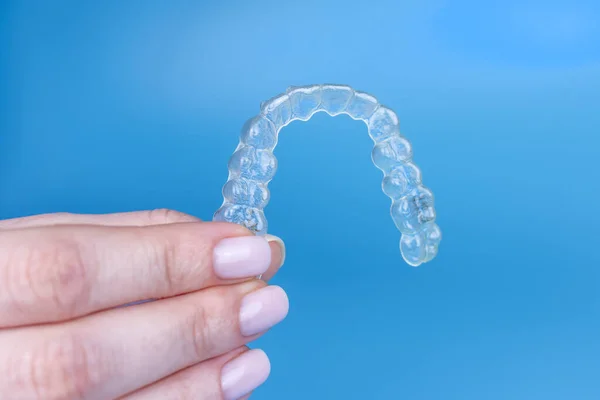 Hand holding removable invisible transparent aligner invisalign or plastic orthodontic braces retainer on blue background — Stock Photo, Image