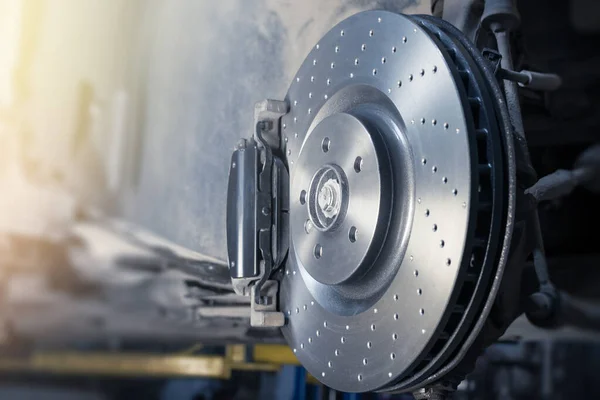 Installation de nouveaux disques et plaquettes de frein perforés sur une automobile moderne dans un atelier automobile. Effet flou. Photo De Stock