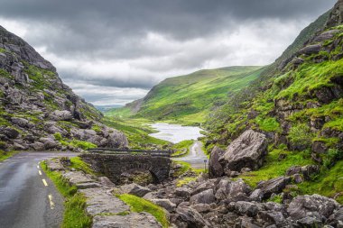 Kara Vadi 'de Dunloe vadisi ve göl manzaralı dar, dolambaçlı yol ve taş köprü, Kerry Halkası, İrlanda