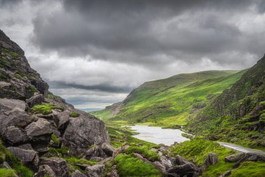 Yeşil dağ tepelerinde panoramik manzara ve Dunloe Gap 'de bir göl. Kara Vadi 'de dramatik fırtınalı gökyüzü, Kerry Halkası, Kerry İlçesi, İrlanda