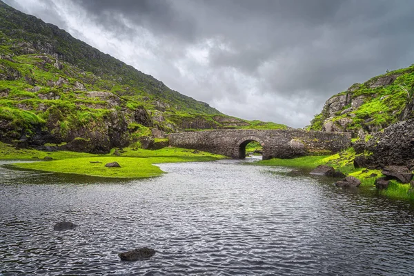 Yeşil vadideki göl üzerindeki küçük taş dilek köprüsü Kara Vadi 'deki Dunloe Geçidi, Kerry Halkası, Kerry İlçesi, İrlanda
