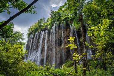 Uzun şelalenin üzerindeki su çizgileri güneş ışığıyla aydınlanır doğal olarak dallarla çerçevelenir. Plitvice Lakes Ulusal Parkı Hırvatistan 'daki UNESCO Dünya Mirası