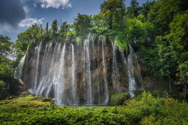 Güneş ışığıyla aydınlatılan büyük şelaleden gelen su izleri. Plitvice Gölleri Ulusal Parkı 'ndaki yemyeşil verimli orman UNESCO Dünya Mirası, Hırvatistan