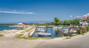 Zaton Körfezi 'nde demirli tekneleri olan küçük bir marina. Adriyatik Denizi 'nin turkuaz sularında eğlenen aileler, arka planda Dinarik Alpler ve Hırvatistan
