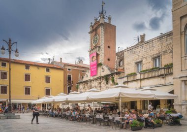 Zadar, Hırvatistan, Temmuz 2019 Açık hava restoranında dinlenen turistler ve arka planda Aziz Lawrence Kilisesi ile eski kent meydanındaki bira bahçesi