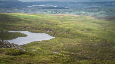 View from Cuilcagh Mountain on lakes, green meadows and fields with patches of sunlight in the valley below, Northern Ireland clipart