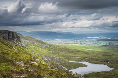Cuilcagh Dağ Parkı 'nda güneş ışığıyla aydınlanan yeşil alanlar ve büyük kayalar.