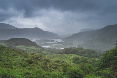 Atmosferik, dramatik fırtına gökyüzü ve bulutlar, İrlanda ikonik bakış açısıyla sisli ve şiddetli yağmur, Bayanlar Görünümü. Göllü yeşil vadi. Kerry Pisti, İrlanda